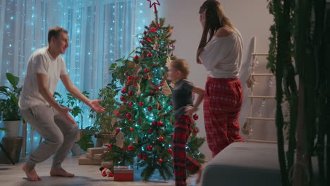 Mom-and-son-decorate-the-Christmas-tree-in-the-living-room-of-their-house-and-cuddle-all-together-with-his-father-after-the-completion-of-the-scenery.-Happy-family-in-pajamas-on-Christmas-Eve.-High-quality-4k-footage